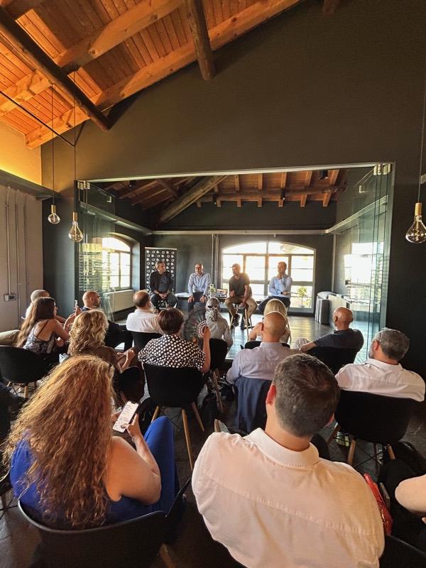 Audience seated facing the speakers in a room with exposed beams