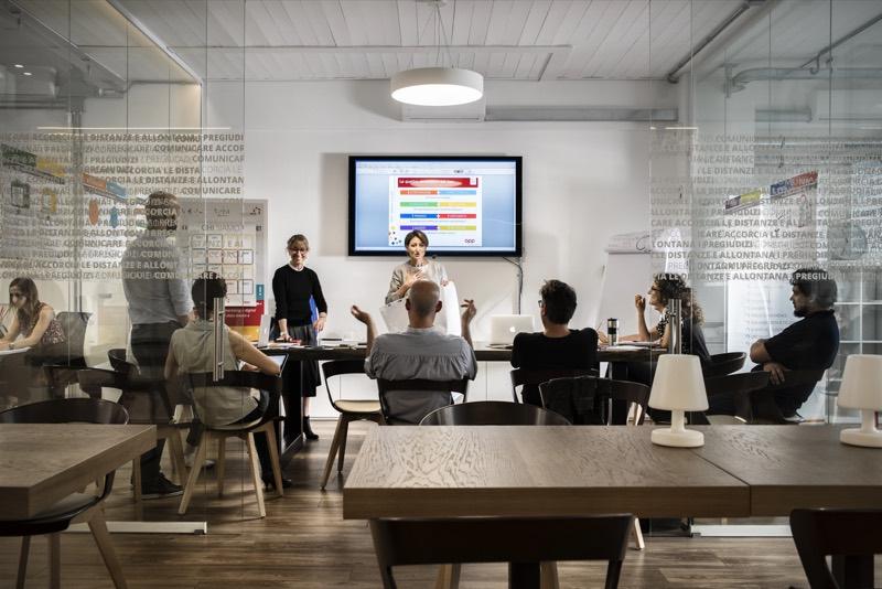 A speaker presents in front of a screen in a meeting room